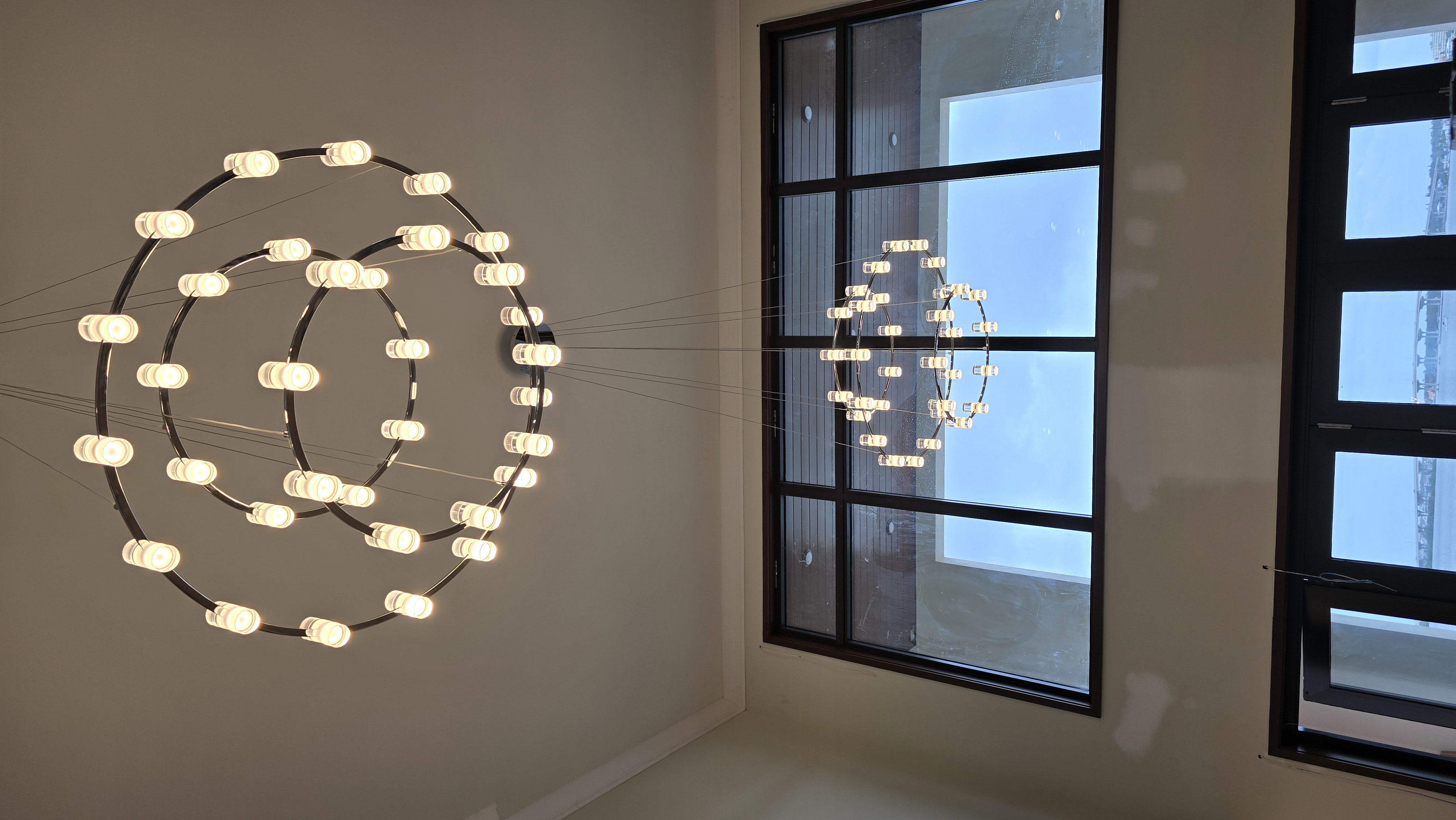Concentric ring LED chandelier mounted beside floor-to-ceiling windows